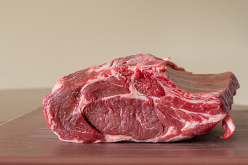 A closeup of a large fresh prime rib beef roast that is sitting on a brown plastic cutting board in a restaurant. The juicy raw red meat has some white fat marbling and multiple rib bones.