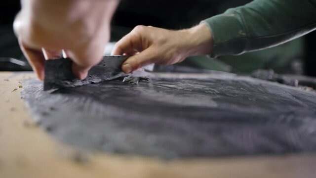 master is designing model from black modeling clay, spreading it on table in workshop