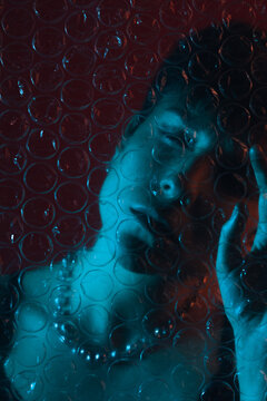 Portrait of a woman behind plastic bubble wrap with her eyes closed