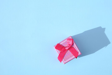 Small pink gift box with ribbon. Minimal composition on pastel blue  background.