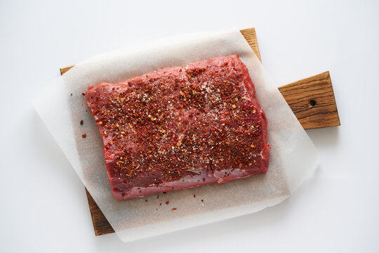 Big whole piece of raw beef meat, striploin on white parchment paper on craft background, zero waste packing. Steak with seasoning and salt. Top view, close up