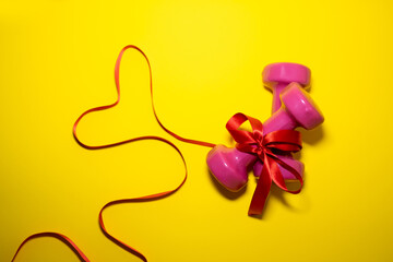 Two pink dumbbells are tied with a red ribbon. Valentine's day concept, sport for lovers. Healthy lifestyle, giving gifts, love sports. Fashionable color yellow