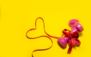 Two pink dumbbells are tied with a red ribbon. Valentine's day concept, sport for lovers. Healthy lifestyle, giving gifts, love sports. Fashionable color yellow