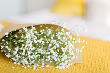 White gypsophila flowers bouquet lying on bed with yellow knitted plaid in bedroom. Happy Valentines Day, Mothers Day, Birthday gift. Beautiful background. Selective focus. Copy space