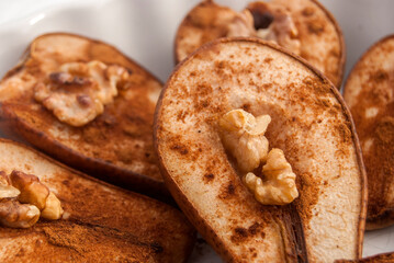 Baked pears with cinnamon powder and walnut core closeup as food background