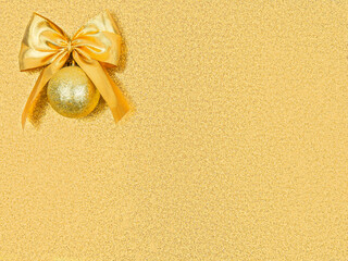 Close up gold bow with christmas ball in upper corner,rectangle shiny shimmering golden sequined backdrop,copy space.Promotion gift to first customer.New Year,birthday decor.Surprise,holiday pattern