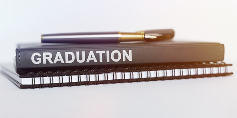 On the table are a notebook, a pen and a book. The book says -GRADUATION