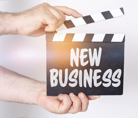 On a white background, a man holds a clapperboard in his hands on which it is written - NEW BUSINESS