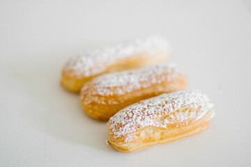 Home made cake eclairs on a white table with sugar powder. Traditional eclairs, profitroles classic, eclairs french.