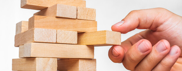 Planning, risk and strategy in business, businessman gambling placing wooden block on a tower. The tower from wooden blocks and man's hand take one block