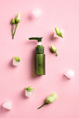 Natural face lotion in green dispenser bottle with ice cubes and flowers on pink background. Skincare concept.