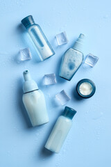 Wet cosmetic bottles and jar with ice cubes on blue background. Set of skin moisturizing beauty products. Flat lay, top view.