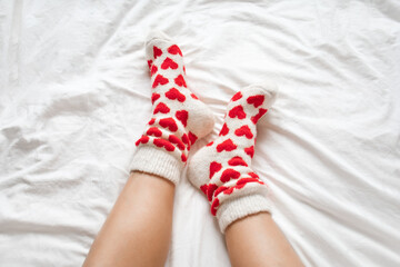women's feet in warm socks with red hearts on a white bed