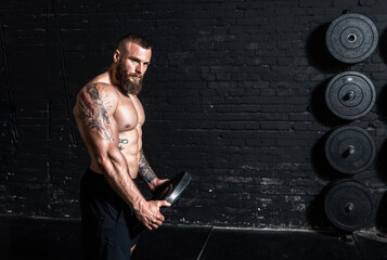 Young active sweaty strong muscular fit man with big muscles holding heavy barbell weight plate in...