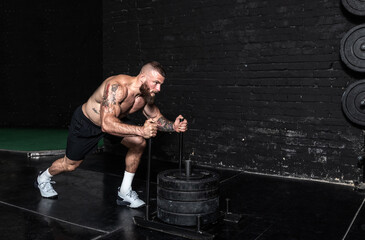 Young strong active sweaty muscular fit man with big muscles pushing heavy weight plates on the...