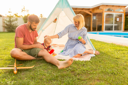 Mother And Father Camping With Their Baby Boy In The Backyard By The Swimming Pool