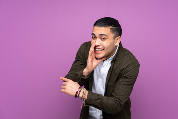 Asian handsome man isolated on blue background pointing to the side to present a product and whispering something