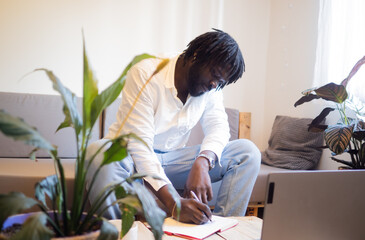 Afro man writing with a pen in a notebook in an office
