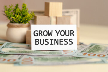 GROW YOUR BUSINESS text on white paper, on the background of money bills and wooden blocks, business concept