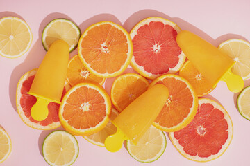 Fruit orange ice lolly and slices of orange, lime and grapefruit on pink background.