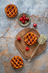 Flat lay of three cherry pies on a textured blue and rustic background, wooden board and serving utensil