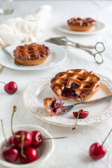 Side view of three individual cherry pies white plates with one pie cut open with a fork, white background and cherries around