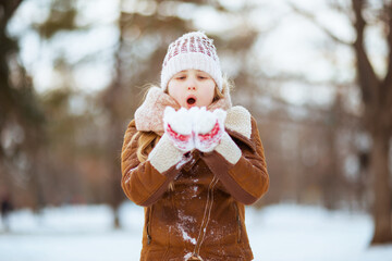 modern girl blowing snow outside in city park in winter