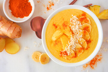 Pineapple, turmeric and ginger smoothie bowl. Top view scene on a white marble background. Healthy...