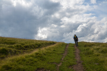 Hiker man with backpack travelling behind the horizon on hiking trail above the clouds. Discover and adventure concept