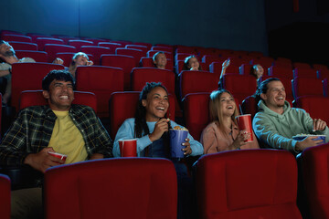 A group of happy diverse friends laughing while watching movie together, sitting in cinema auditorium