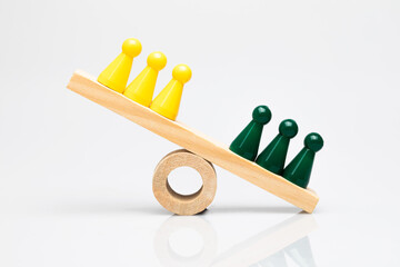 Green and yellow game pieces on a wooden seesaw. Conceptual shot around comparison, competition of...
