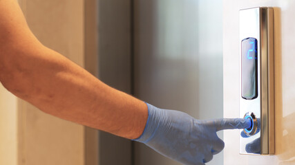Female hands in medical protective gloves pressing elevator button. Young woman touches lift buttons. Disease prevention during quarantine, hygiene. Close up. © Red Stock