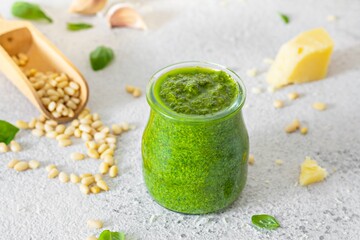 Green pesto in a glass jar made from fresh basil leaves, pine nuts, parmesan, garlic and olive olia on a light background. Popular Italian dressing for salads, pasta and pizza.