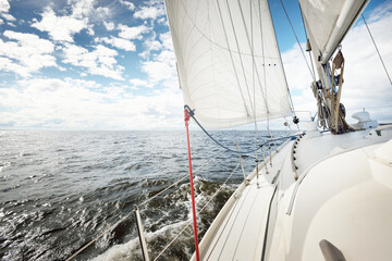 White sloop rigged yacht sailing in an open sea on a clear day. A view from the deck to the bow....