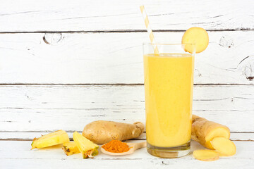 Pineapple, turmeric and ginger smoothie against a white wood background with ingredients. Healthy immune boosting, weight loss, anti-inflammatory.