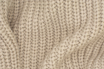 Background from natural fabric. Very soft knitted of beige color with stripes and folds. The surface of cotton corrugated blanket for warming in cold weather.