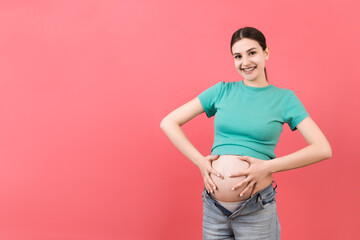 pregnant woman dressed in opened jeans scratching her belly at colorful background with copy space. Problem of stretch marks concept