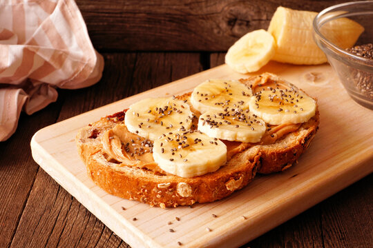 Healthy Breakfast Toast With Peanut Butter, Bananas And Chia Seeds On Multi Grain Bread. Close Up On A Dark Wood Background.