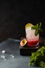 Refreshing cocktail with vodka,soda,berry puree,lime,mint,passion fruit and crushed ice in fine crystal glass on wooden box and dark background.Close up of cooling cocktail.