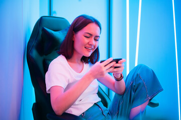 Cybersport gamer playing mobile game on the smart phone sitting on a gaming chair in neon color...