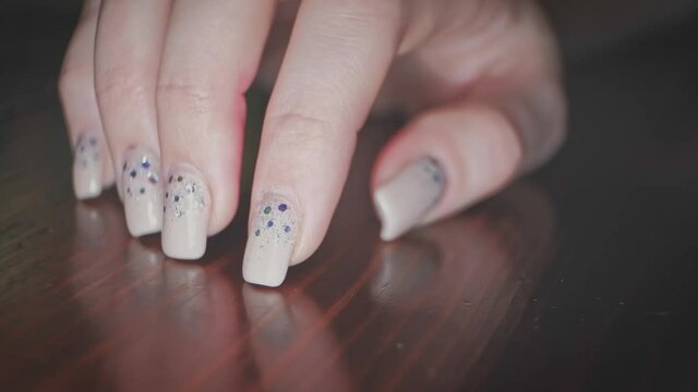 Girl taps her nails with exotic manicure on polished table countertop
