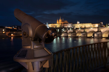 Fototapeta na wymiar city ​​binoculars and railings and in the blurred background Charles Bridge and Prague Castle in the center of Prague in Podvece