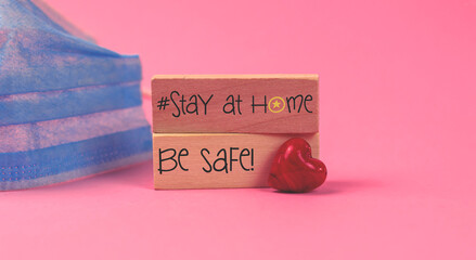 Stay home concept with a medical mask on a pink bakground, with wooden blocks, tetxt inscription and red heart, valentine's day holidays
