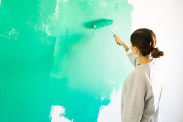 Beautiful woman painting the walls with a paint roller