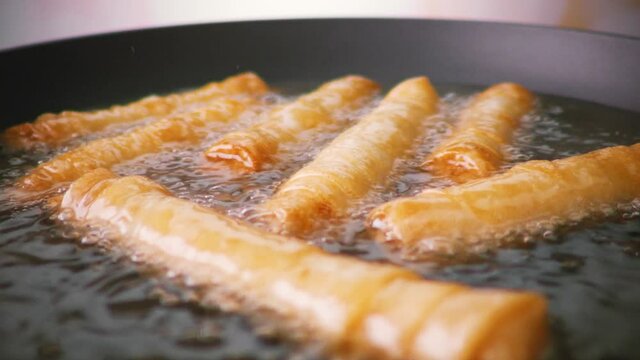 Preparation of the national Turkish dish sigara boregi. Rolls of dough fried in a frying pan in oil. Slow motion.