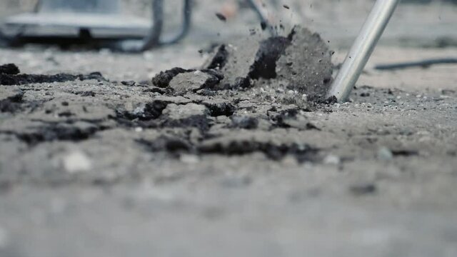 Chisel of a demolition hammer breaking asphalt and throwing chunks in slo-mo