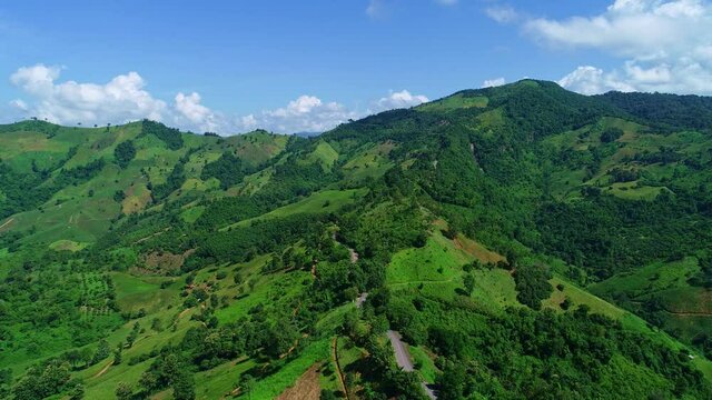 Aerial top view of sky road over top of mountain with farmland green jungle forest in sunny summer day at Pua district Nan province Thailand Beautiful nature video for background