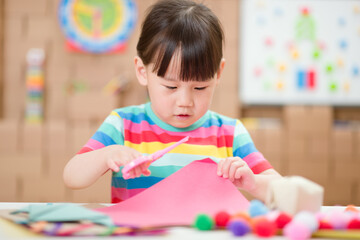 young girl using scissors cutting papper for making craft for homeschooling
