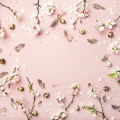 Easter holiday background. Flat-lay of tender Spring almond blossom flowers on branches, feathers, quail eggs over light pink background, top view, copy space, square crop. Greeting card concept