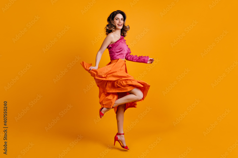 Wall mural Merry european woman in bright skirt dancing. Studio shot of positive brunette girl.